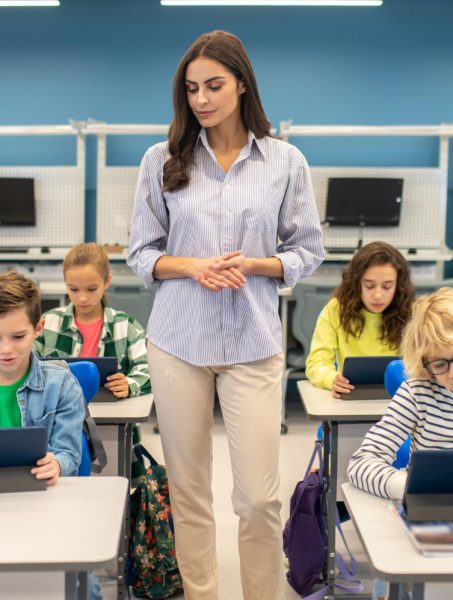 woman-standing-watching-students-working-tablets